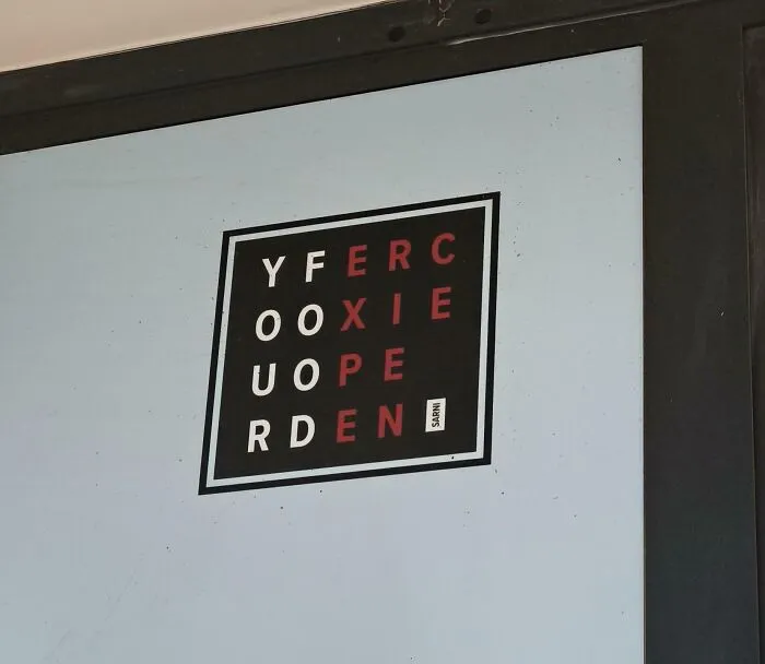 A terribly designed sign on a square window decal with confusing jumbled letters in black and red