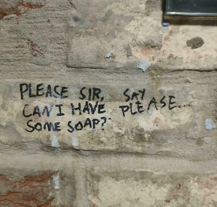 Handwritten text on a stone wall asking for soap, featuring confusing and terribly designed signs layout.