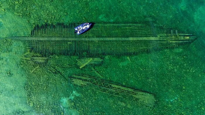 Aerial view of a boat floating directly above a large shipwreck, showcasing submerged objects in clear green water.