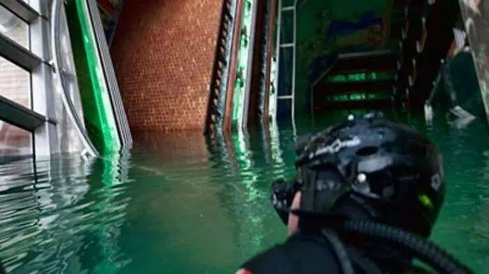 Scuba diver exploring a flooded interior building with green water, showcasing unsettling submerged objects