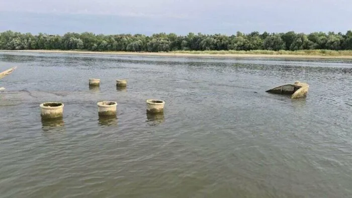 Old concrete structures and a sunken boat partially emerging from river water, depicting submerged objects