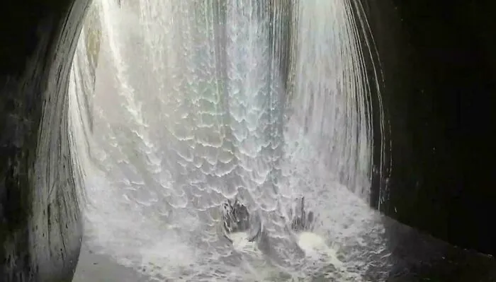 A view inside a dark tunnel flooded with rushing water, displaying unnerving submerged objects and flow