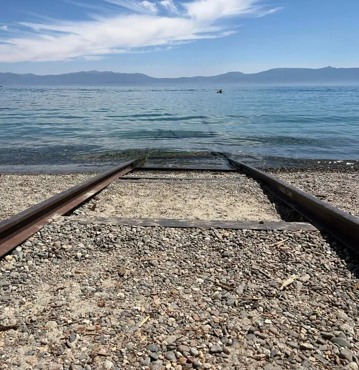 Submerged objects like old train tracks leading straight into a clear lake shore.
