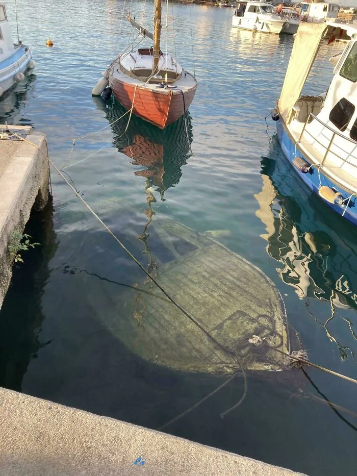 Submerged objects including a small wooden boat resting at the bottom of a harbor.