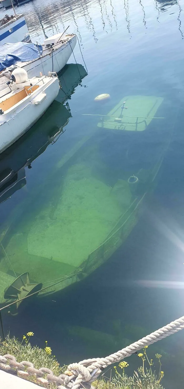 Clear view of a boat submerged underwater near a dock, causing fear of submerged objects.