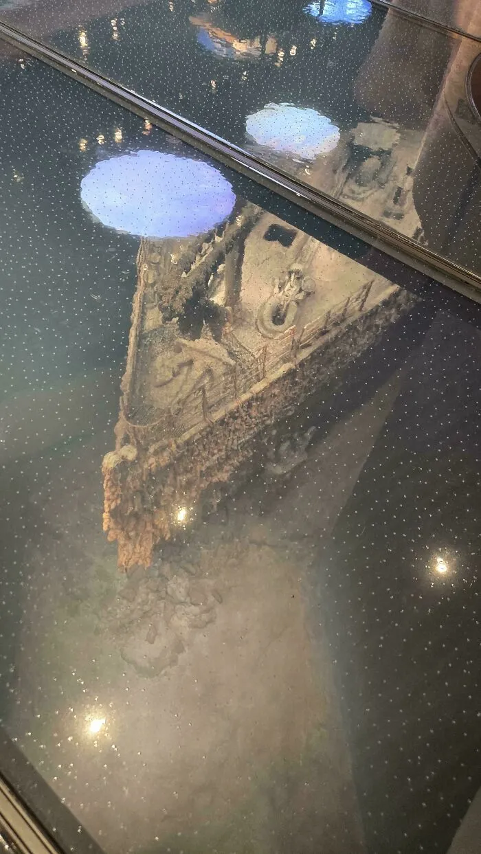 A detailed scale model of a submerged ship bow displayed under a glass floor, evoking submechanophobia.