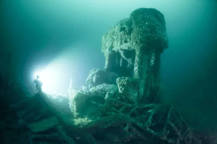 Scuba diver illuminating strange, coral-covered submerged objects deep underwater.