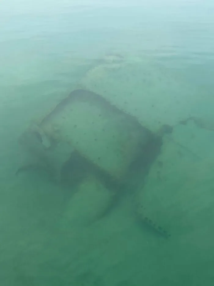 Unnerving photo of a rusting submerged object visible just beneath the surface of murky green water.