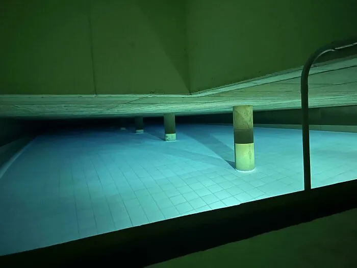 Eerie indoor pool with a low ceiling and submerged pillars, showcasing unnerving submerged structures.