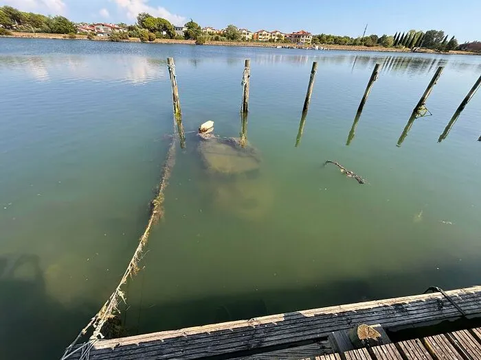 A car sitting among submerged objects just below the clear green water surface next to a wooden pier.