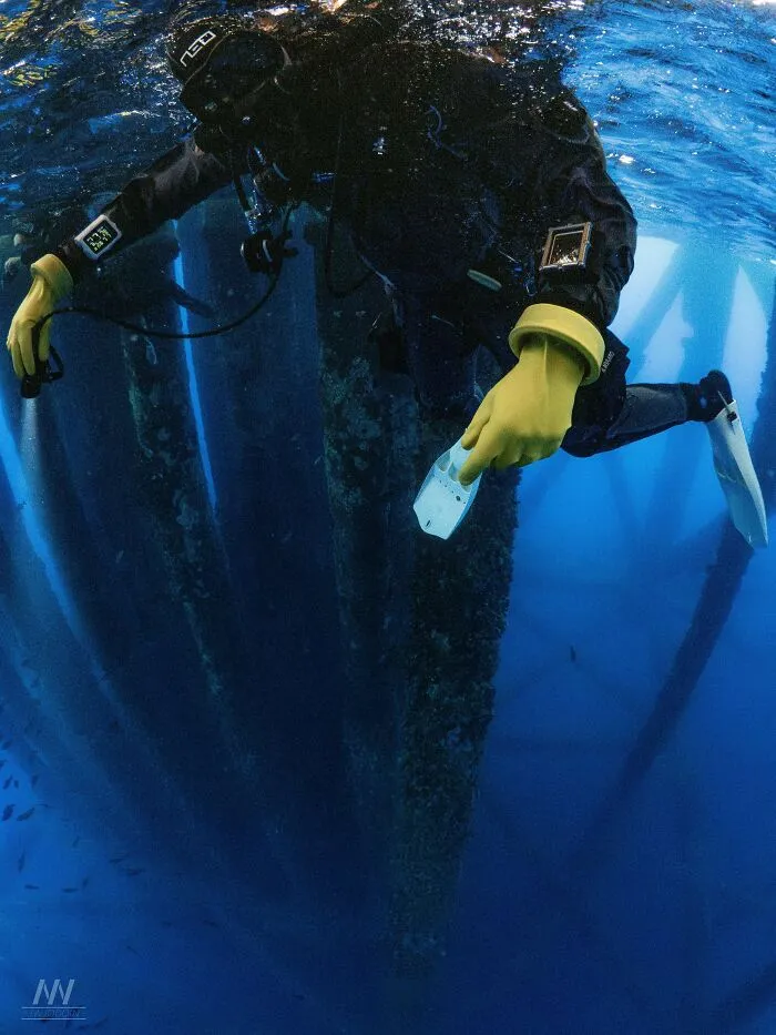 Scuba diver swimming near massive submerged objects supporting an offshore structure.