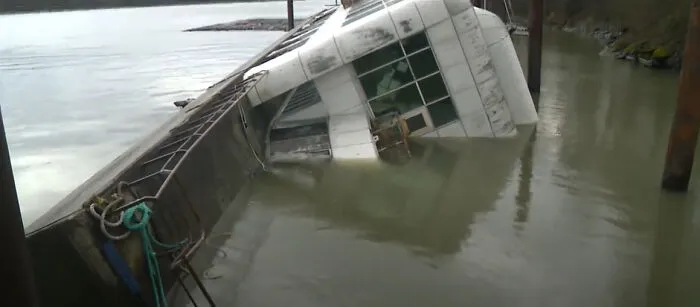 A partially submerged object showing a large white vessel tipping into murky river water