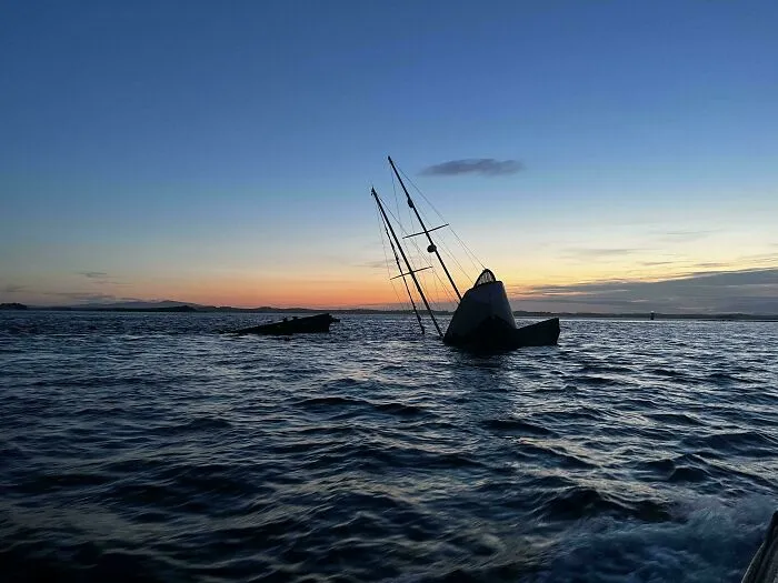 Silhouette of a sunken sailboat, one of many submerged objects, tilting out of the water at sunset.