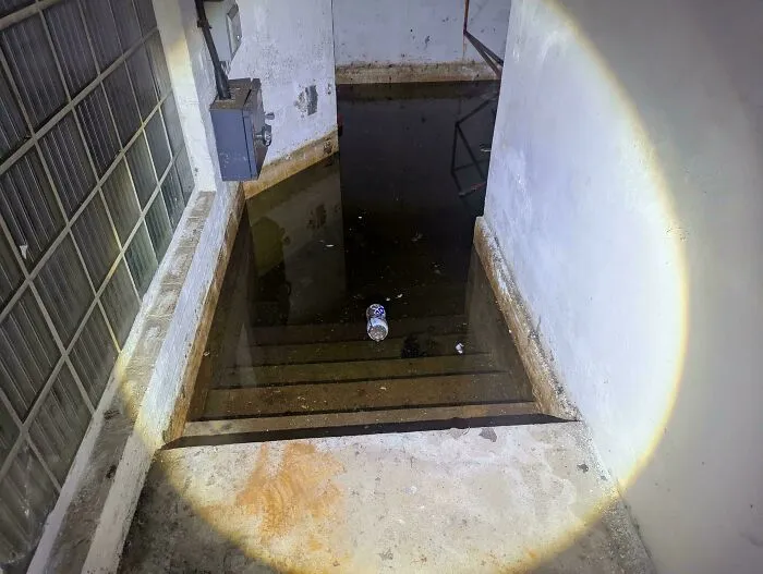 A flashlight beam shining down flooded stairs leading into dark water with submerged objects.