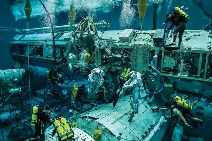 Divers training near complex equipment, capturing fascinating submerged objects in a deep blue pool.