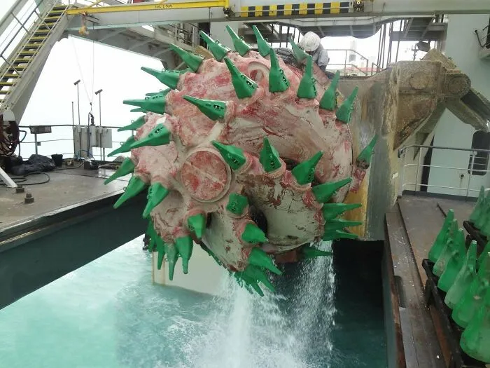 A massive industrial cutter wheel, one of many unnerving submerged objects, dripping water on a ship deck.