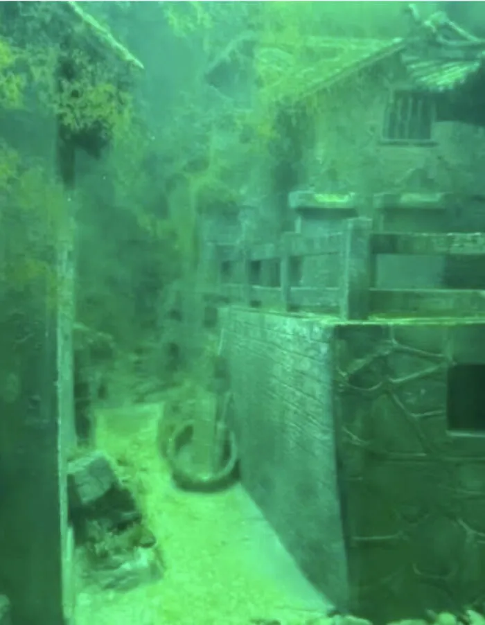An eerie underwater view of ancient submerged structures covered in moss and silt.