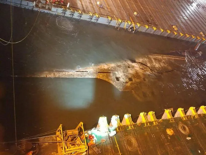 An aerial view at night showing dark murky water and submerged objects glowing under industrial lights.