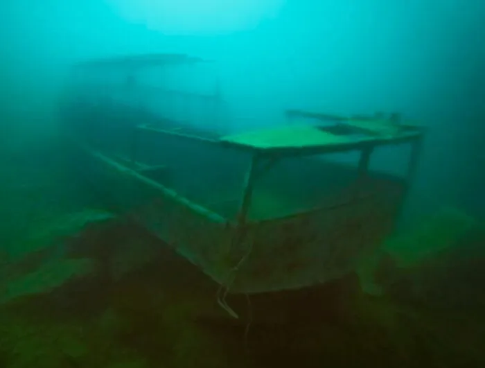 Eerie view of a boat among submerged objects resting on the dark lake floor.