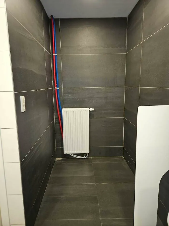 Radiator with exposed red and blue pipes in a tiled room, highlighting construction fails.