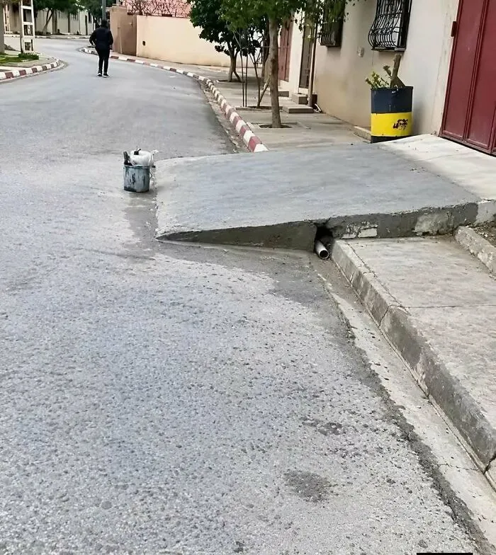 A steep concrete driveway ramp built directly over a sidewalk curb, showing obvious construction fails.