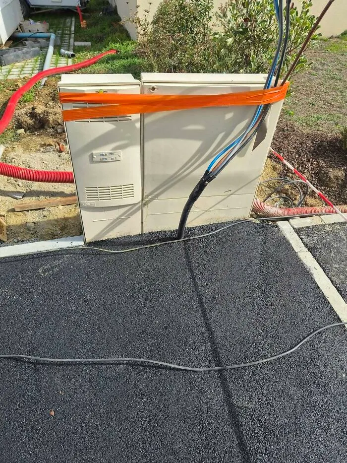 Electrical utility boxes bound with orange tape and asphalt paved directly over exposed cables in construction fails.