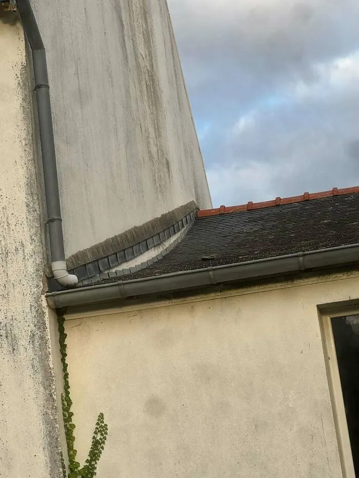 Outdoor downspout draining directly onto a lower roof surface showcasing construction fails.