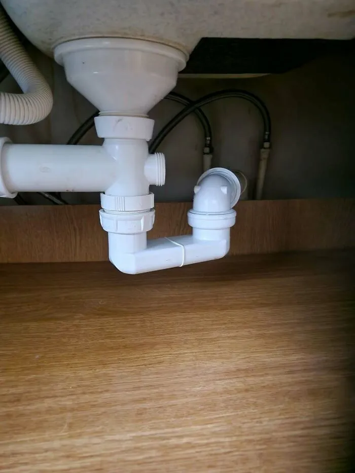 Disconnected plastic plumbing pipes under a sink showing a major construction fail.