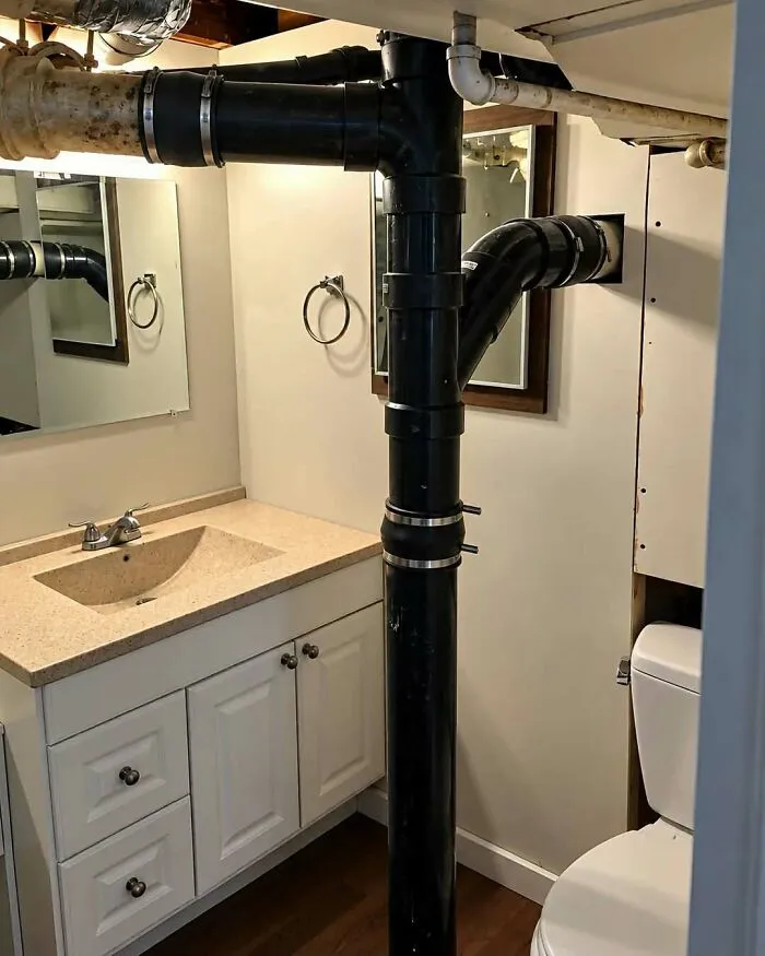 A black plumbing pipe running straight through the middle of a bathroom as an example of construction fails.