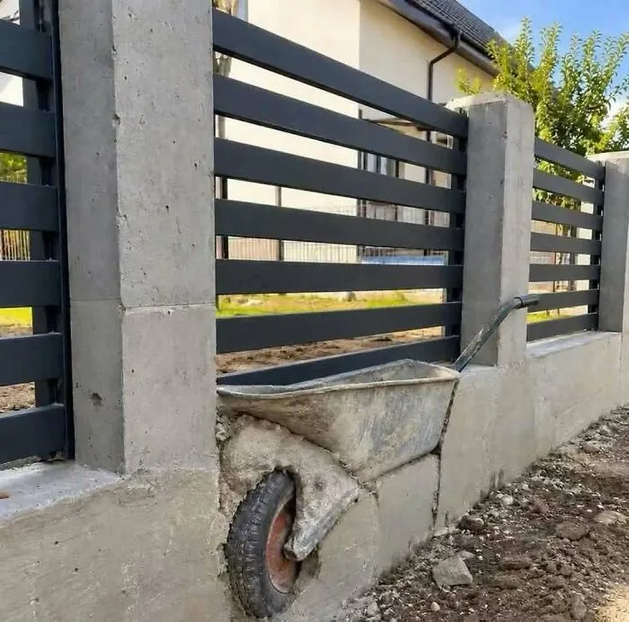 Metal wheelbarrow permanently embedded into concrete fence wall in a hilarious construction fail.