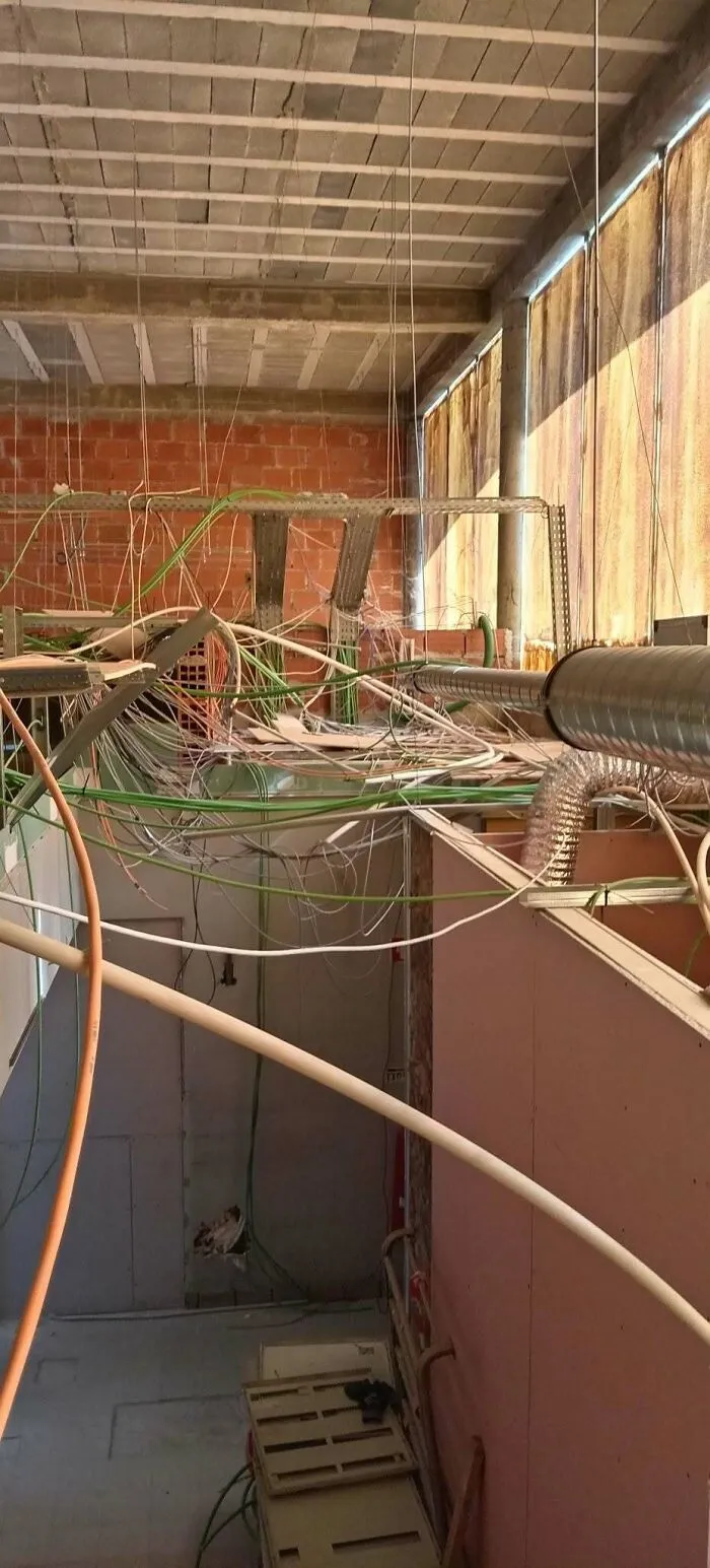 Messy exposed wires and ducts hanging from the ceiling showing extreme construction fails.