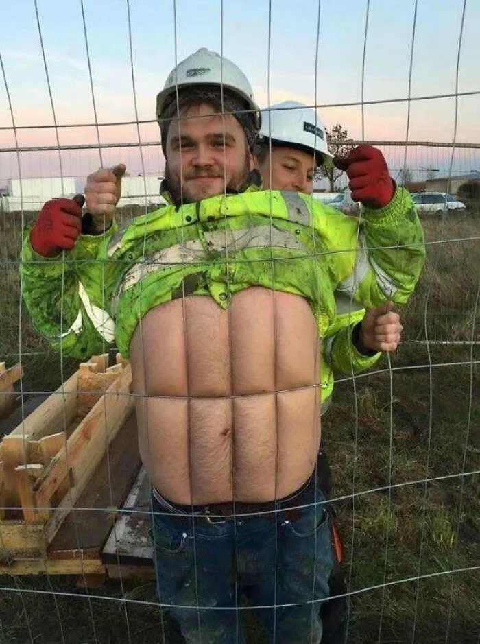 Construction worker pressing his stomach against a wire fence for a funny photo.