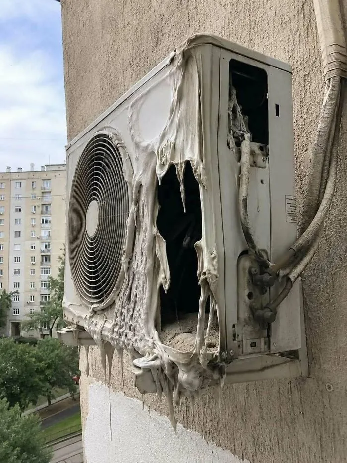A melted air conditioner unit hanging on a wall, showcasing extreme heat damaged construction fails.