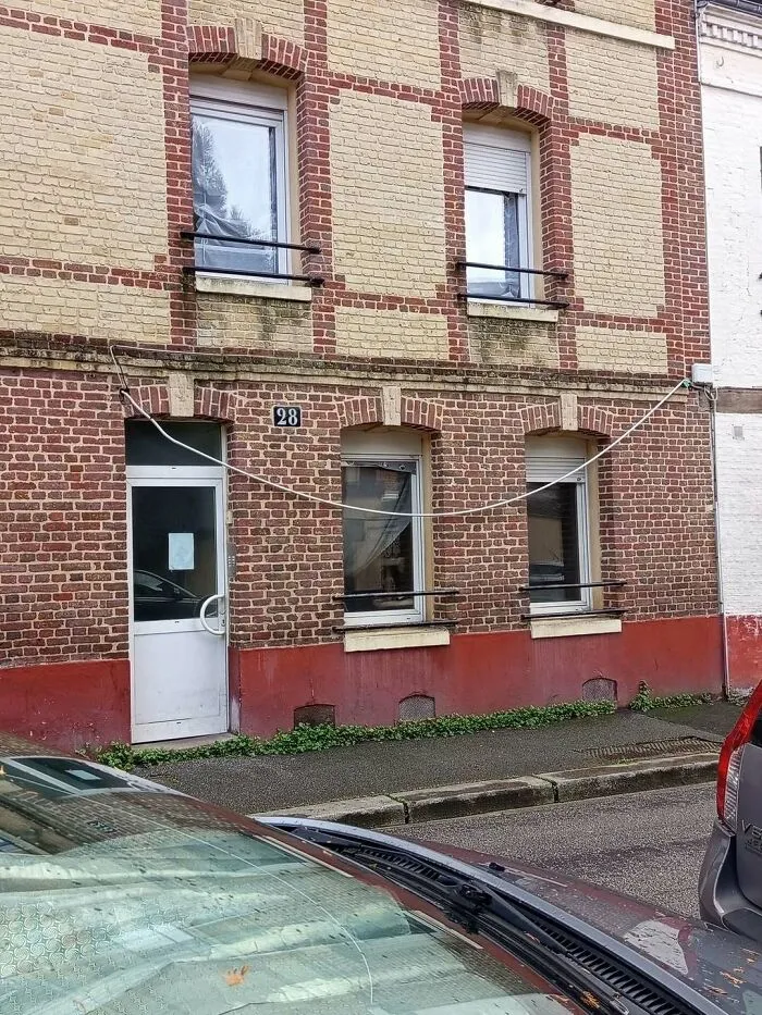 An exterior brick building wall with a poorly routed white wire hanging loosely, demonstrating clear construction fails.