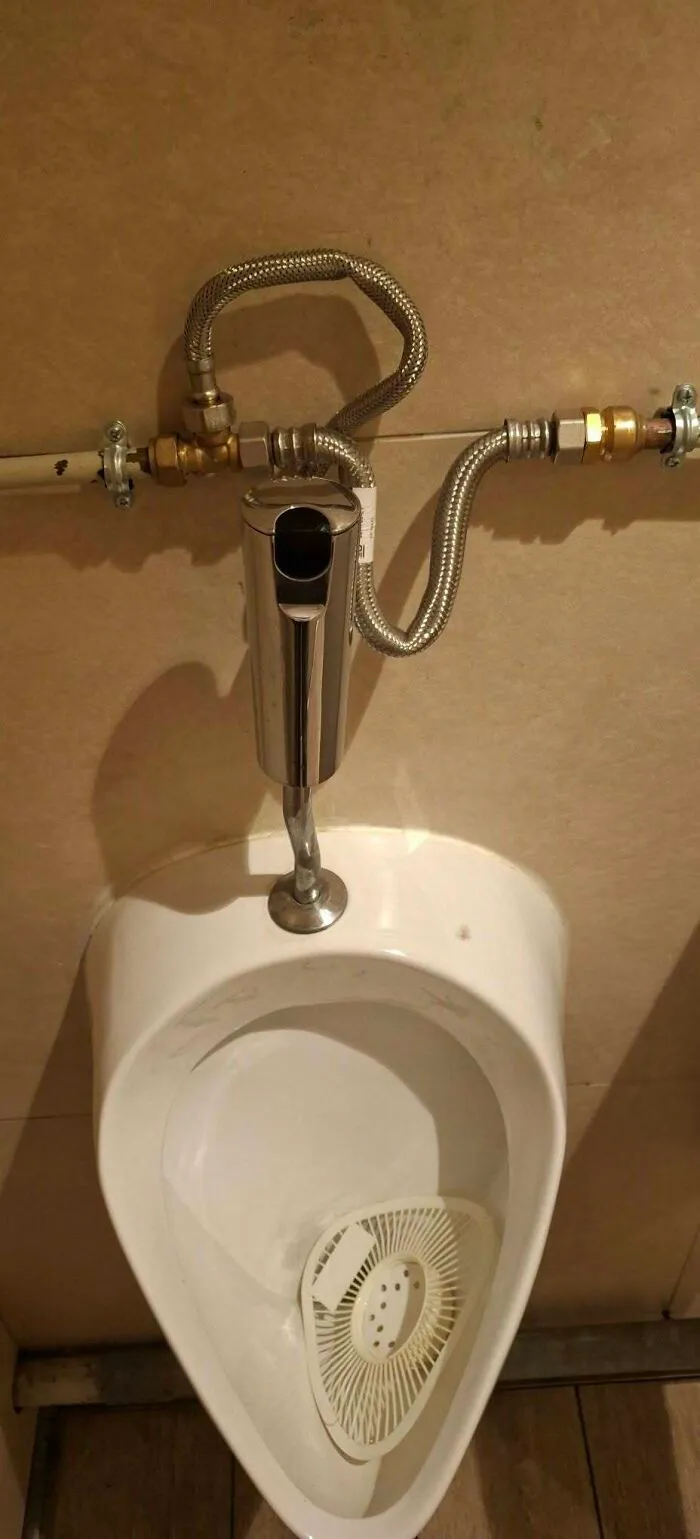 A urinal with convoluted and exposed flexible plumbing pipes, illustrating hilarious construction fails.