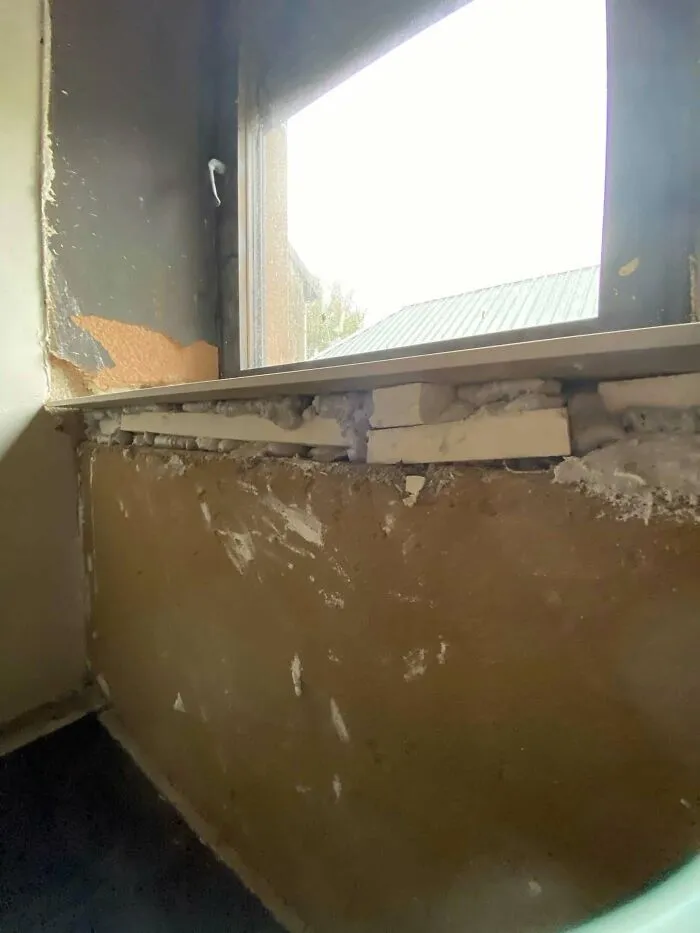 Rough window installation with foam and wooden shims exposed, illustrating a construction fail.