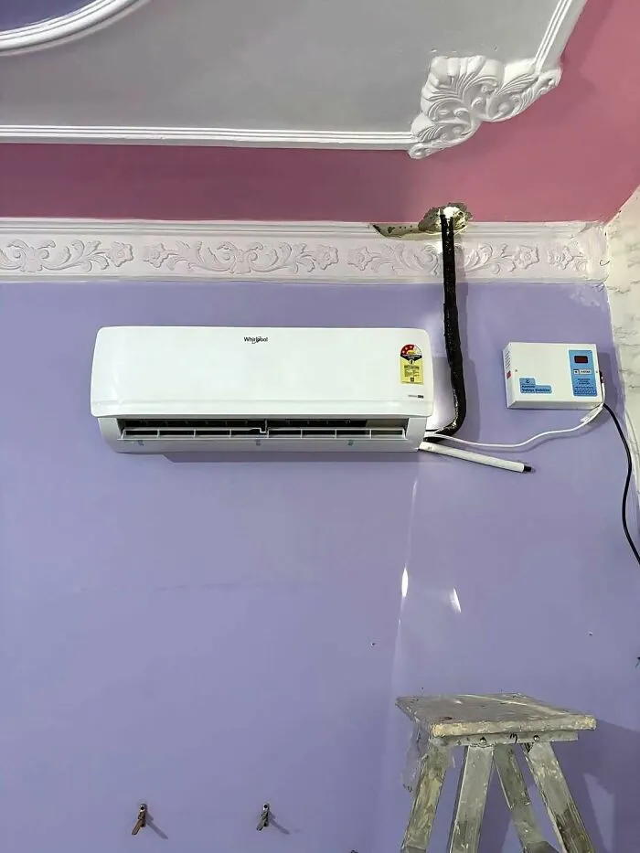 An air conditioner installed with messy exposed wiring through decorative molding, a construction fail.