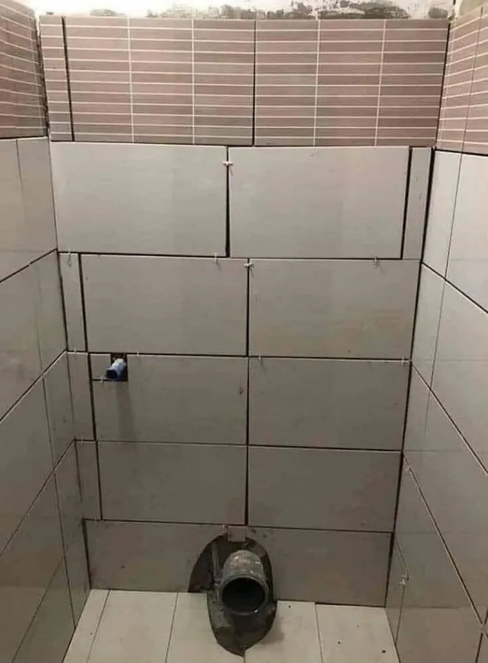 Misaligned wall tiles around plumbing in a bathroom, revealing a major construction fail.