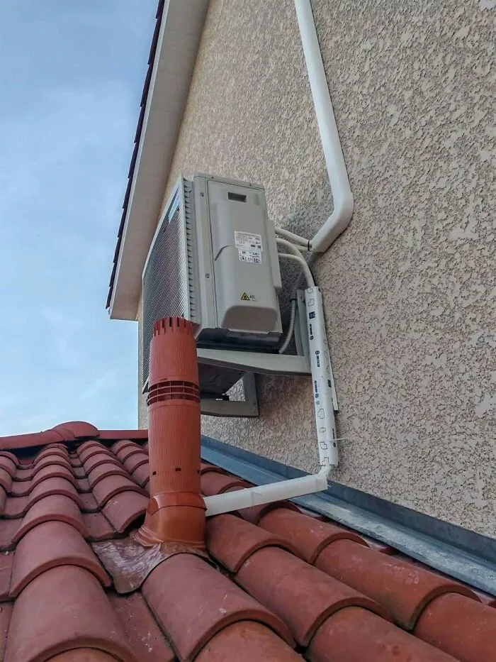 Unusual HVAC installation construction fails with an air conditioner unit mounted awkwardly over a roof vent.