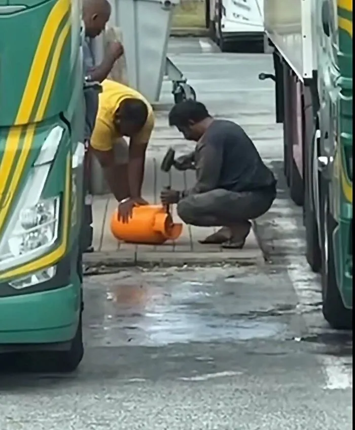 Dangerous construction fails showing workers hammering on a gas cylinder between trucks.