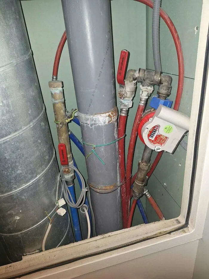 Messy utility pipe setup representing chaotic plumbing and construction fails inside a wall cutout.
