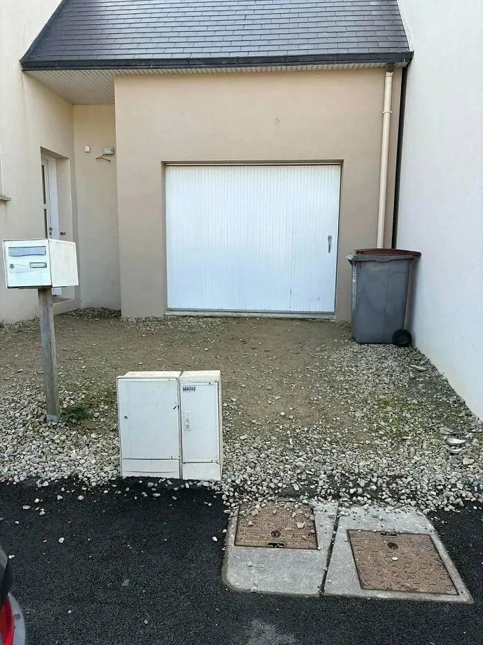A garage door blocked by electrical utility boxes, highlighting a design construction fail.