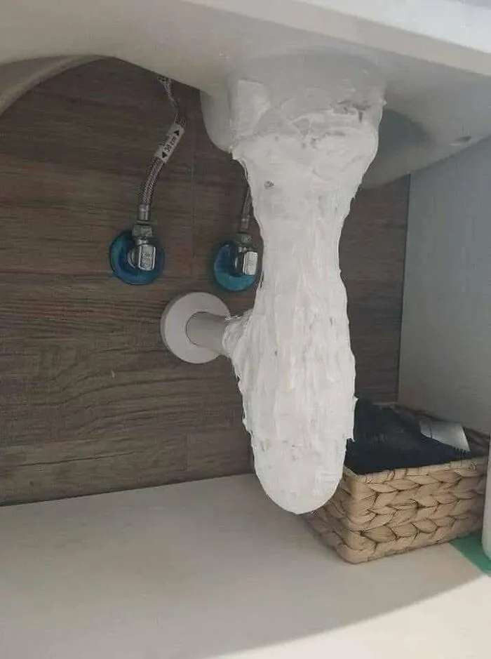 Sink drain pipe covered entirely in messy white sealant, showcasing a major construction fail.