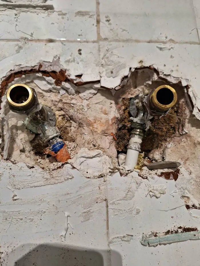Water pipes sticking out of a roughly smashed tiled wall, demonstrating bad construction work.