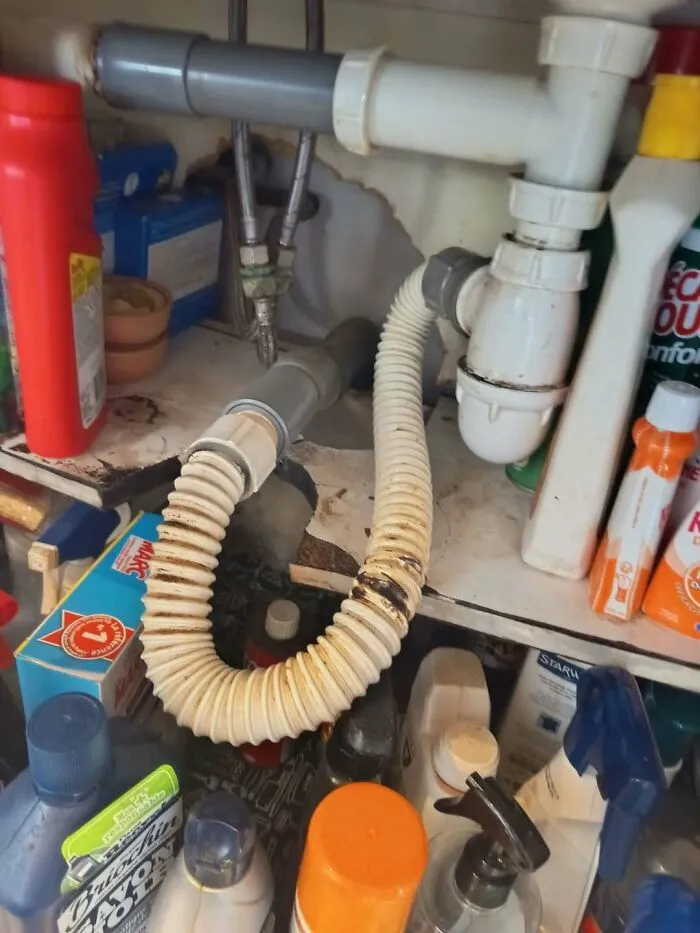 Disorganized and bent flexible plumbing pipes under a sink representing a construction fail.