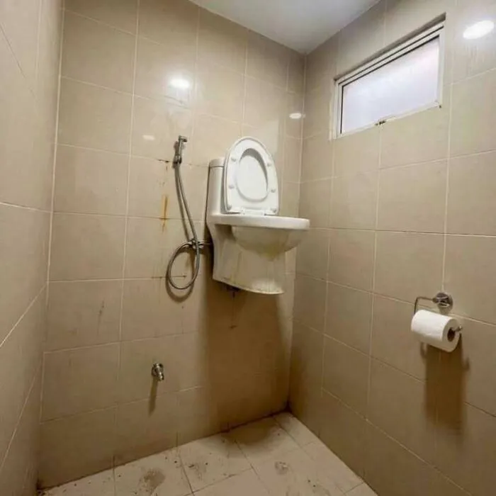 A toilet installed high up on a tiled bathroom wall representing an absurd construction fail.
