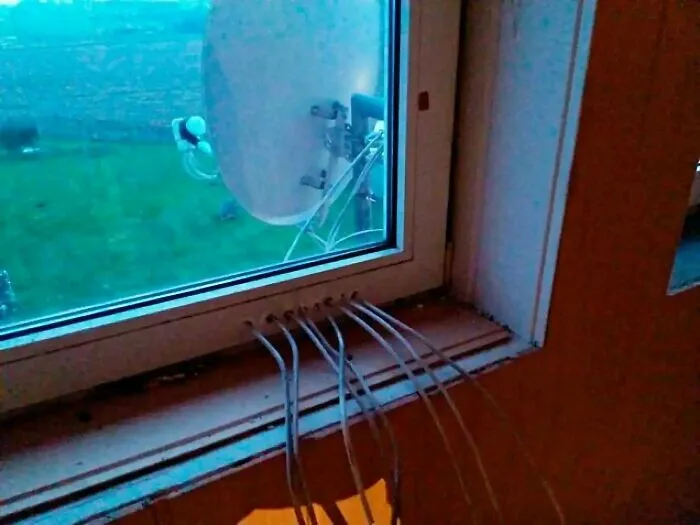 Multiple white wires drilled directly through a window frame in a severe DIY construction fail.
