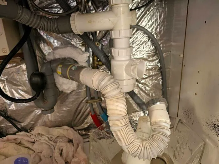 Convoluted plumbing setup under a sink showcasing a terrible plumbing construction fail.