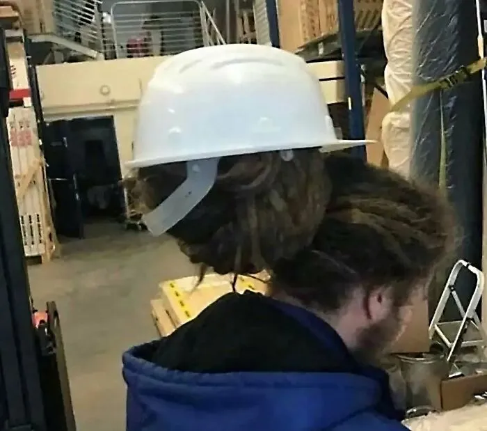 A worker wearing a white hard hat over thick dreadlocks in an unsafe construction fail scenario.