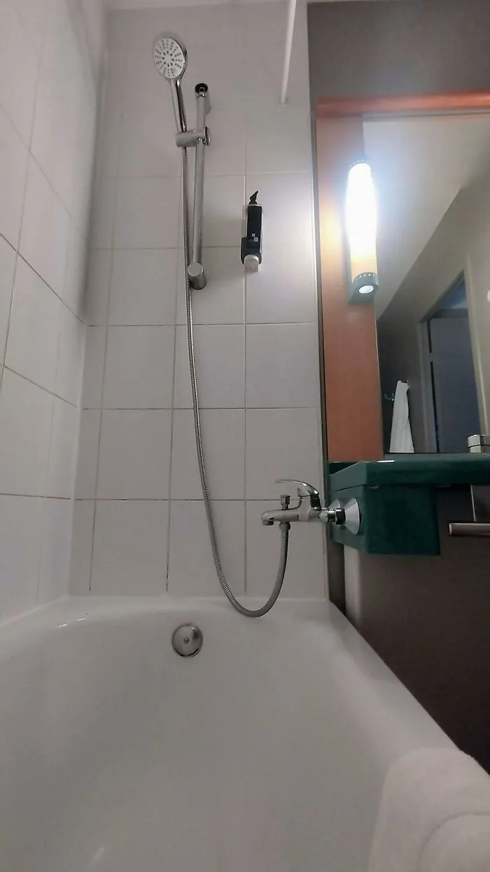 A bathtub faucet awkwardly positioned off-center and dangerously close to the vanity top, showing construction fails.